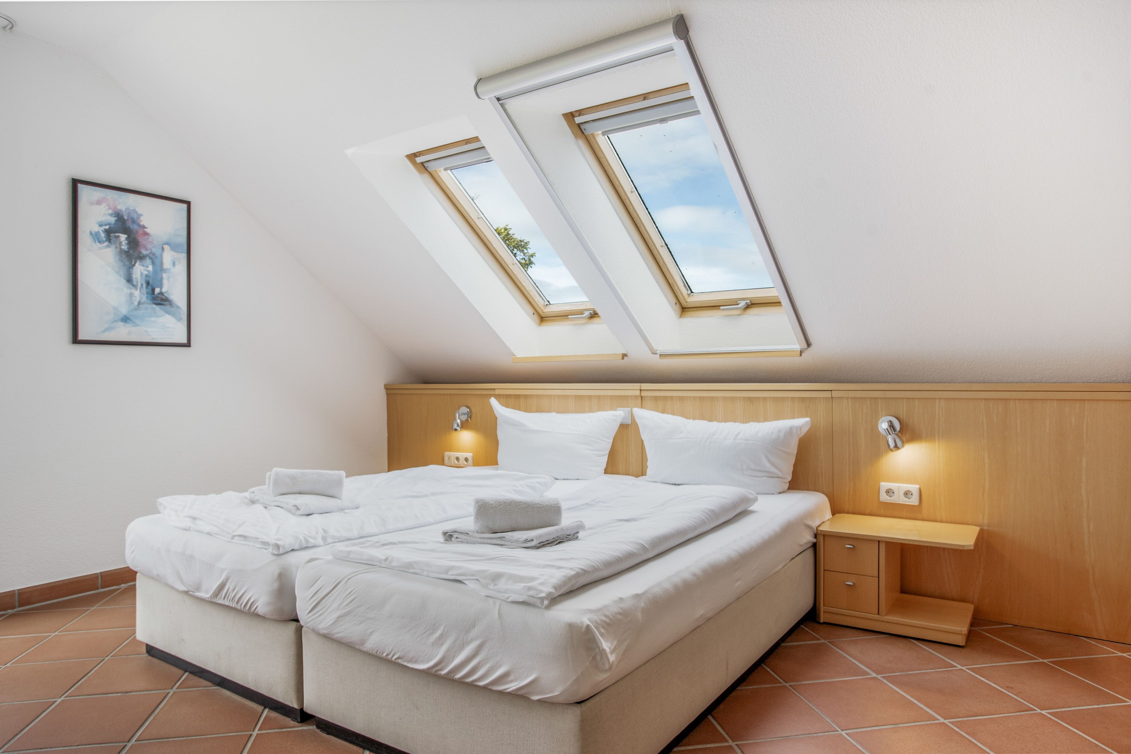 A bedroom with a bed, two bedside tables, a nightstand, and a skylight.