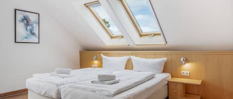 A bedroom with a bed, two bedside tables, a nightstand, and a skylight.