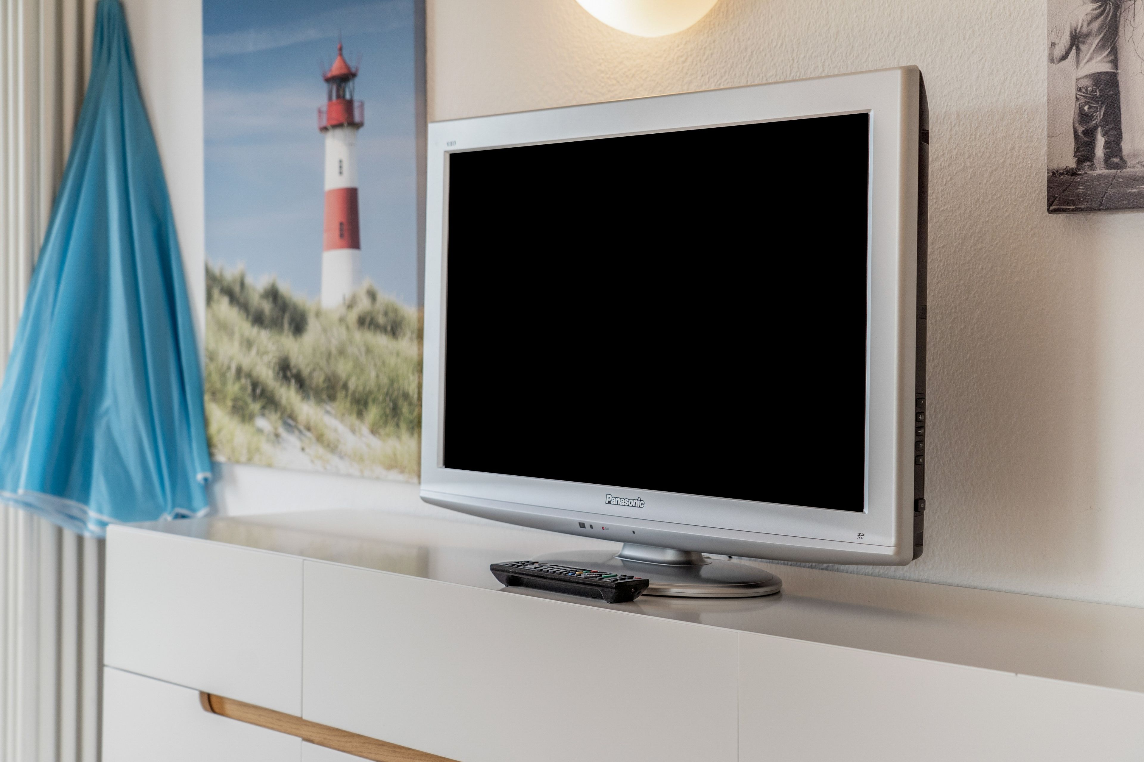 Un téléviseur à écran plat fixé au mur, avec une télécommande posée sur un meuble blanc situé en dessous.