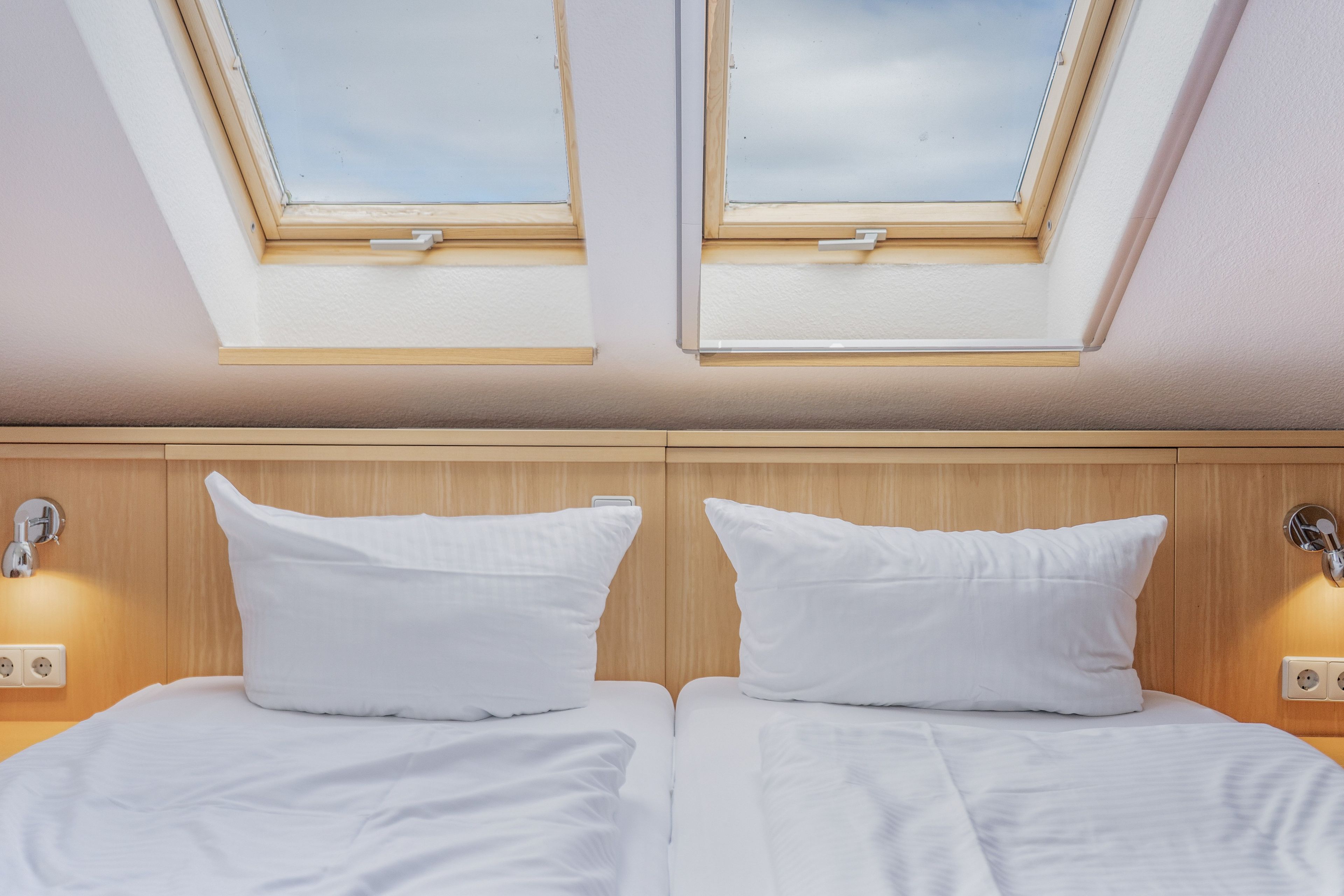 A room with two beds, a skylight, and a wooden headboard.