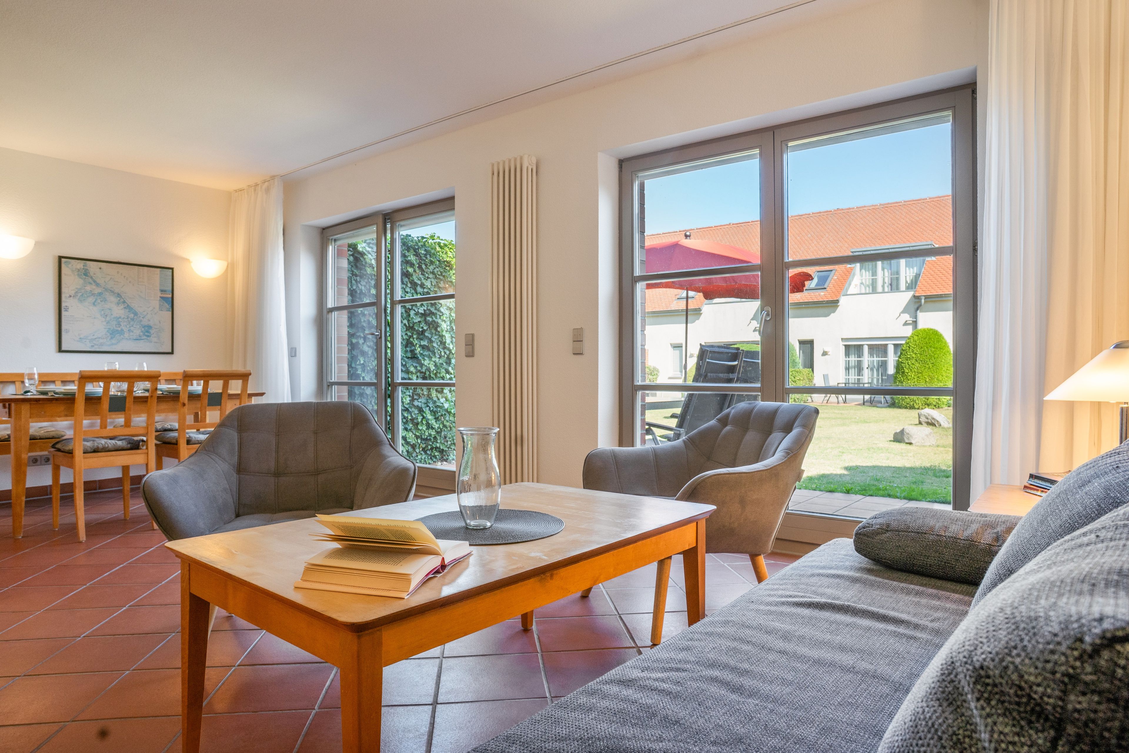 A modern living room with a sofa, chairs, a dining table, and a view of a house through large windows.