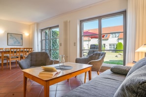 A modern living room with a sofa, chairs, a dining table, and a view of a house through large windows. - Ideal for Families & Pets – "Dream Vacation" Apartment with Terrace (Mellenthin)