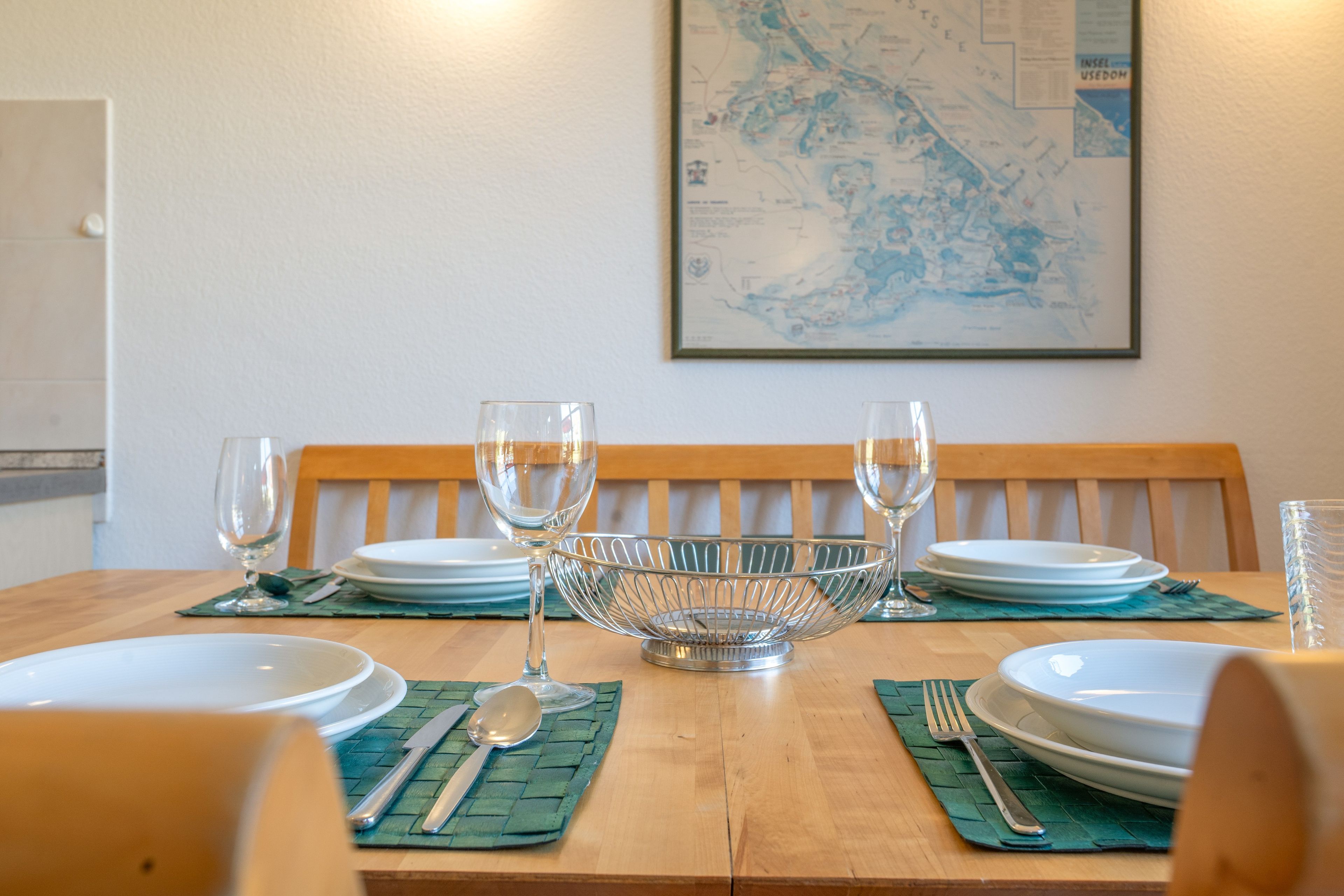 Una mesa de comedor dispuesta con platos, cubiertos y vasos, con un mapa en la pared de fondo.