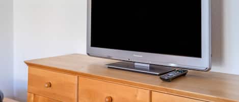 Un téléviseur posé sur un meuble en bois, avec une télécommande à côté.