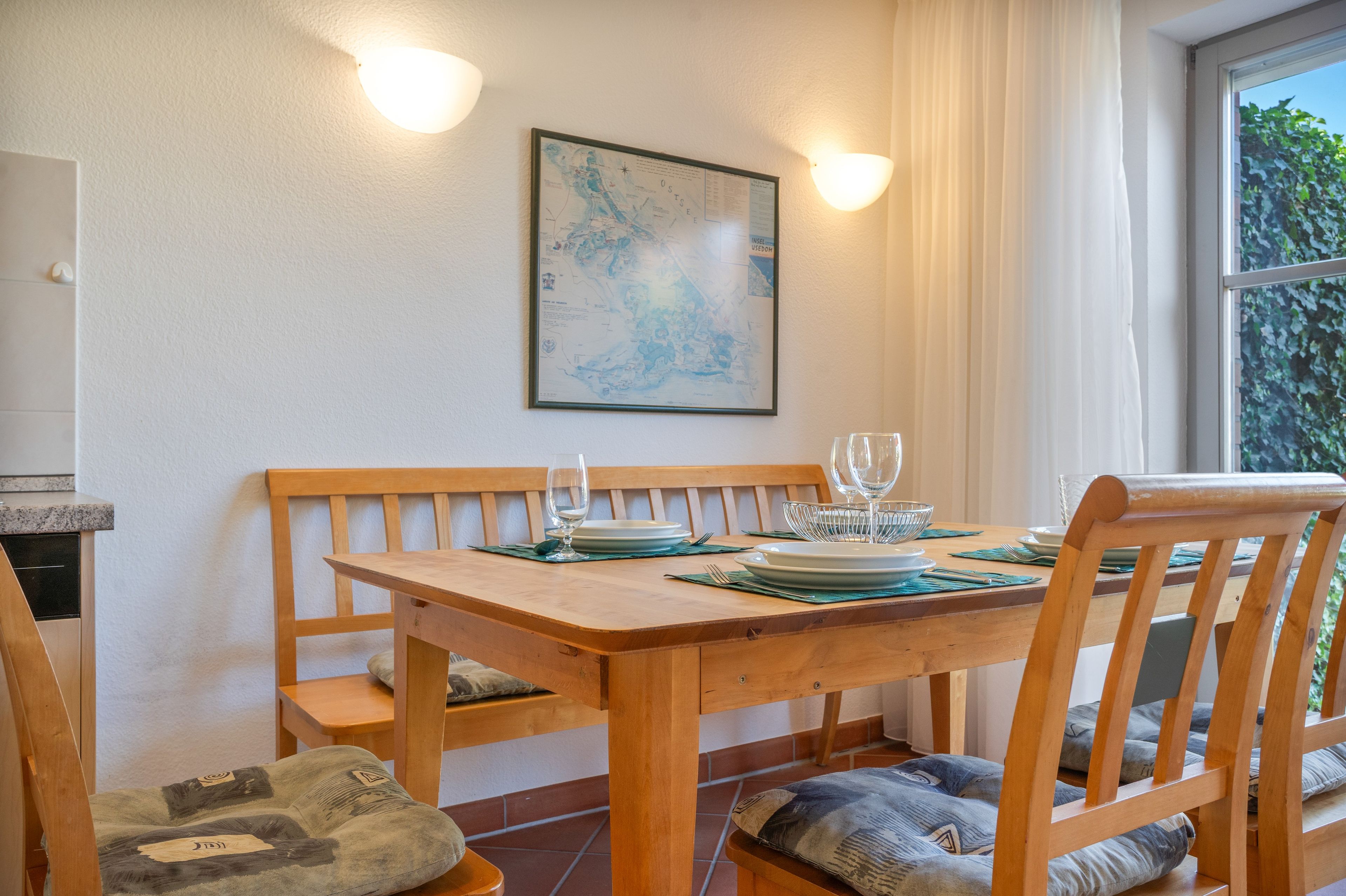 Une table à manger avec des chaises, une carte encadrée accrochée au mur et une fenêtre avec des rideaux.