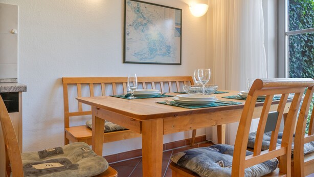 Et spisebord med stole, et kort i ramme på væggen og et vindue med gardiner.