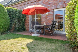Un patio con mesa y sillas, un paraguas rojo y una pared de ladrillo.