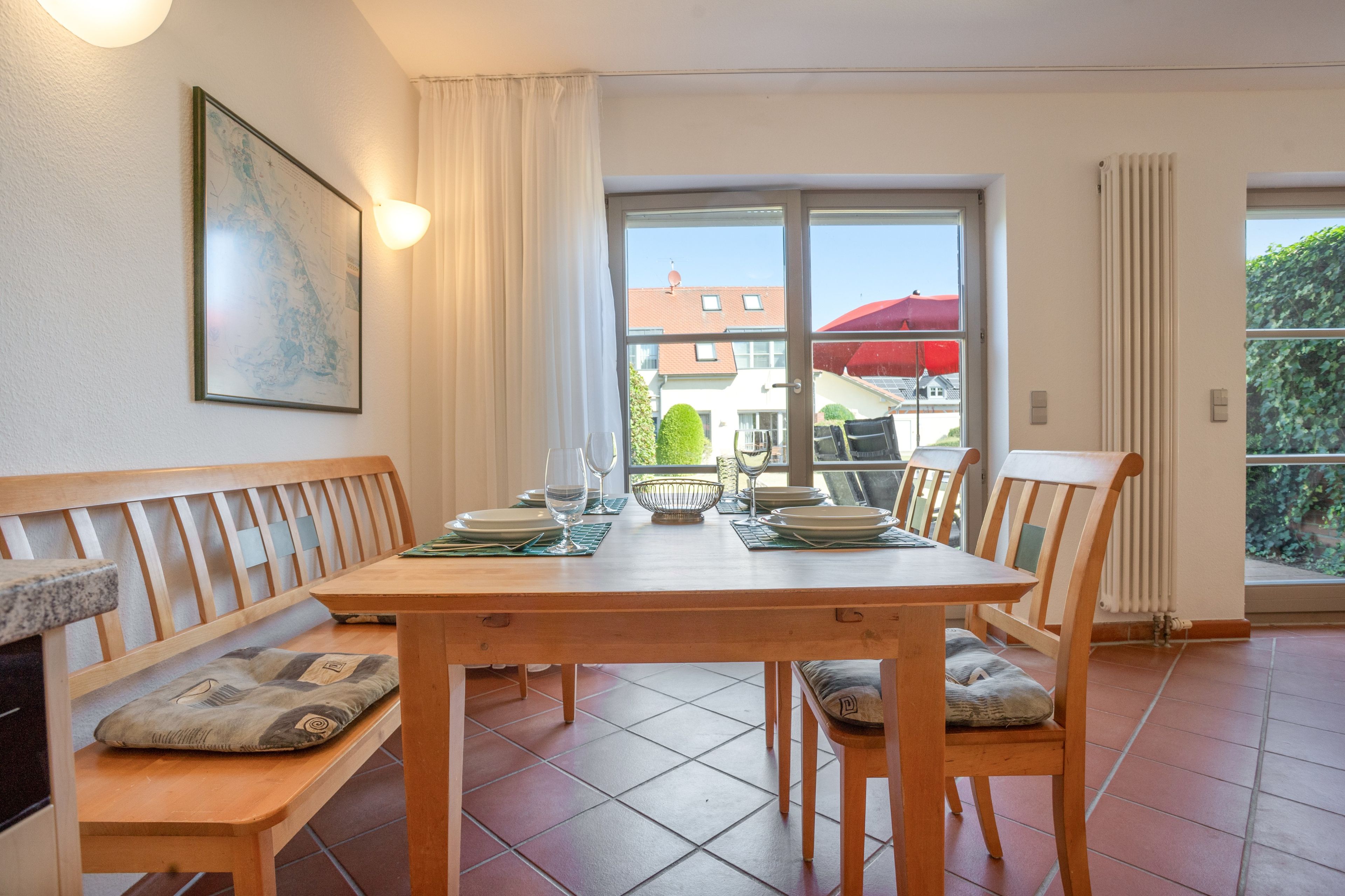 Ein Essbereich mit Holztisch und Bänken, einem großen Fenster mit Vorhängen sowie einem gerahmten Bild an der Wand.