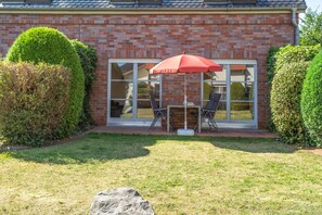 A brick house with a glass door and windows, a red umbrella, and two chairs outside. - Ideal for Families & Pets – "Dream Vacation" Apartment with Terrace (Mellenthin)