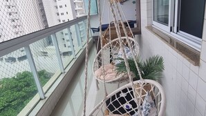 A balcony with two macramé hanging chairs, a potted plant, and a view of a building through a mesh window. - Blue Mar Apartamento (Guarapari)