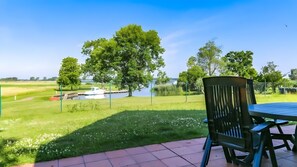 A patio with a table and chairs, a grassy area, a body of water, and trees. - Holiday Apartment "Seeterassen" – 68 m², Two Terraces & View of the Achterwasser (Mellenthin)