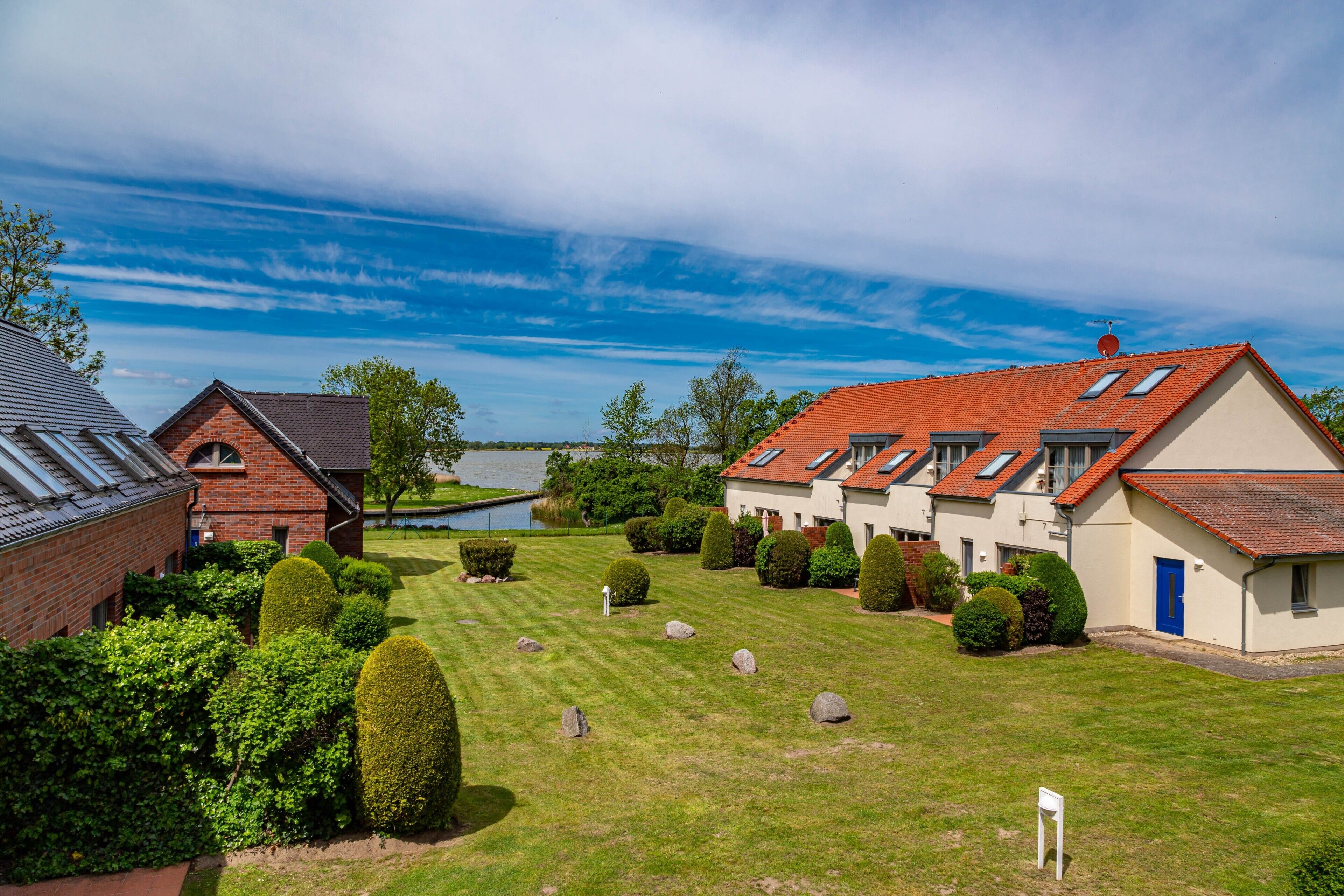 A residential area with multiple houses, a well-maintained lawn, and a body of water in the background.