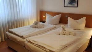 Ett hotellrum med två sängar, vita sängkläder, en sänggavel, ett nattduksbord och en väggmonterad lampa.