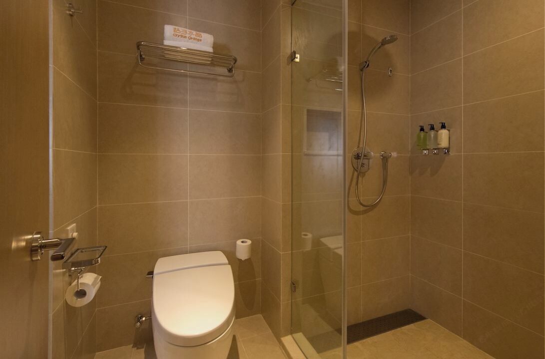 Un baño con inodoro, ducha con mampara de vidrio y repisa con artículos de tocador.