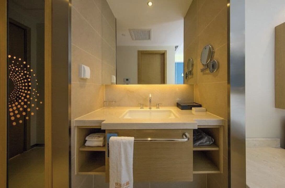A modern bathroom with a large sink, mirror, towel rack, and built-in shelves.