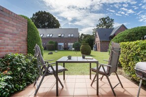 Eine Terrasse mit Tisch und Stühlen, umgeben von Hecken und einer Backsteinmauer.