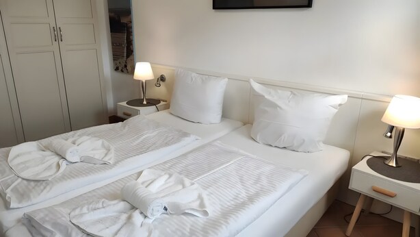 Ein ordentlich bezogenes Doppelbett mit Kissen, zwei Nachttische mit Lampen und ein Kleiderschrank.