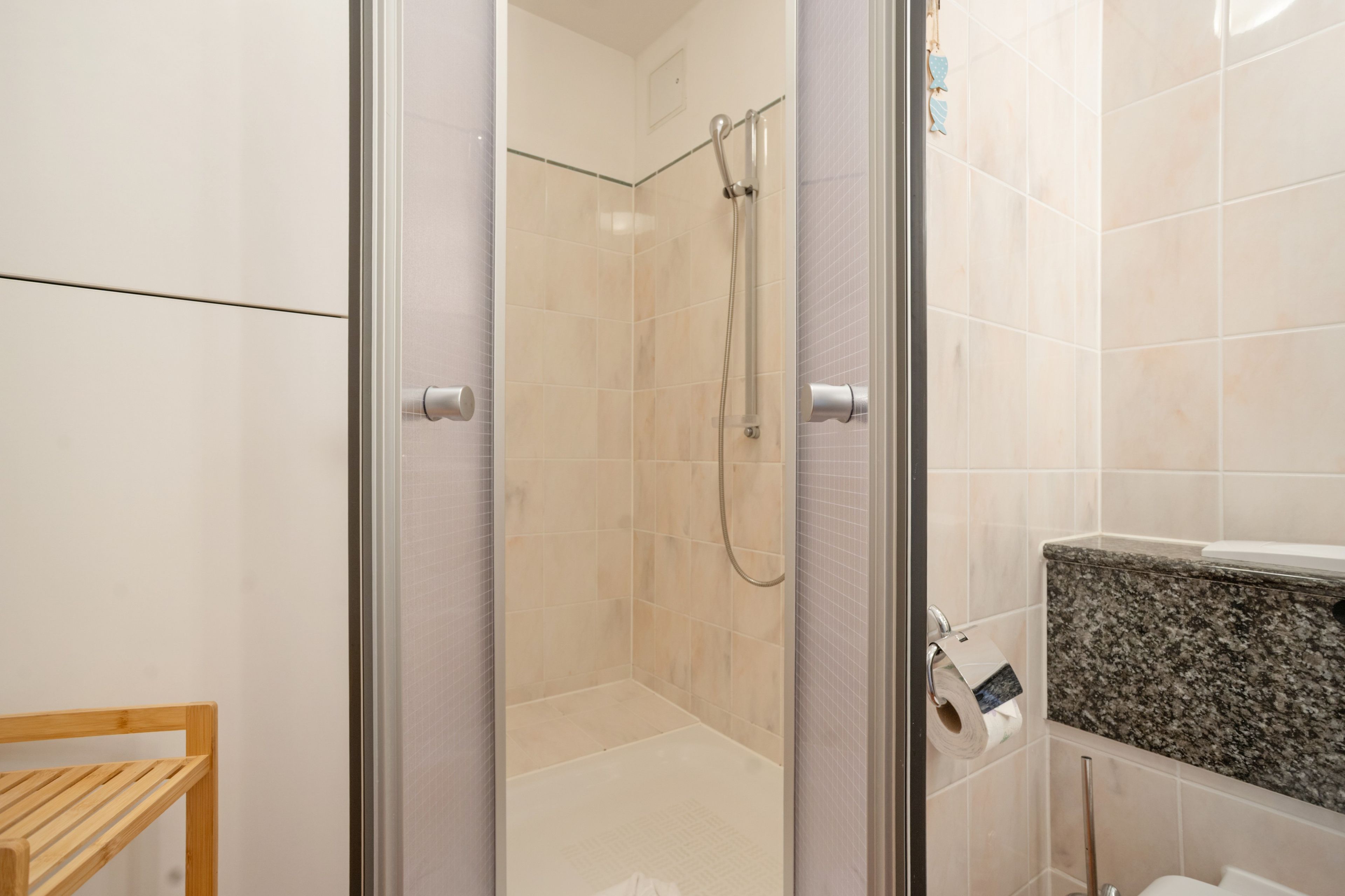 Un baño moderno con cabina de ducha de vidrio, encimera de granito y una silla de madera.