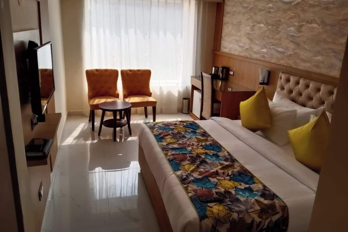 A hotel room with a bed, two armchairs, a small table, a TV, and a window with curtains.