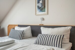 A neatly made bed with striped pillows, a framed abstract painting, and a small decorative item on the wall. - Holiday Apartment "Achterwasser View" – Balcony & Nature in Usedom's Hinterland (Mellenthin)