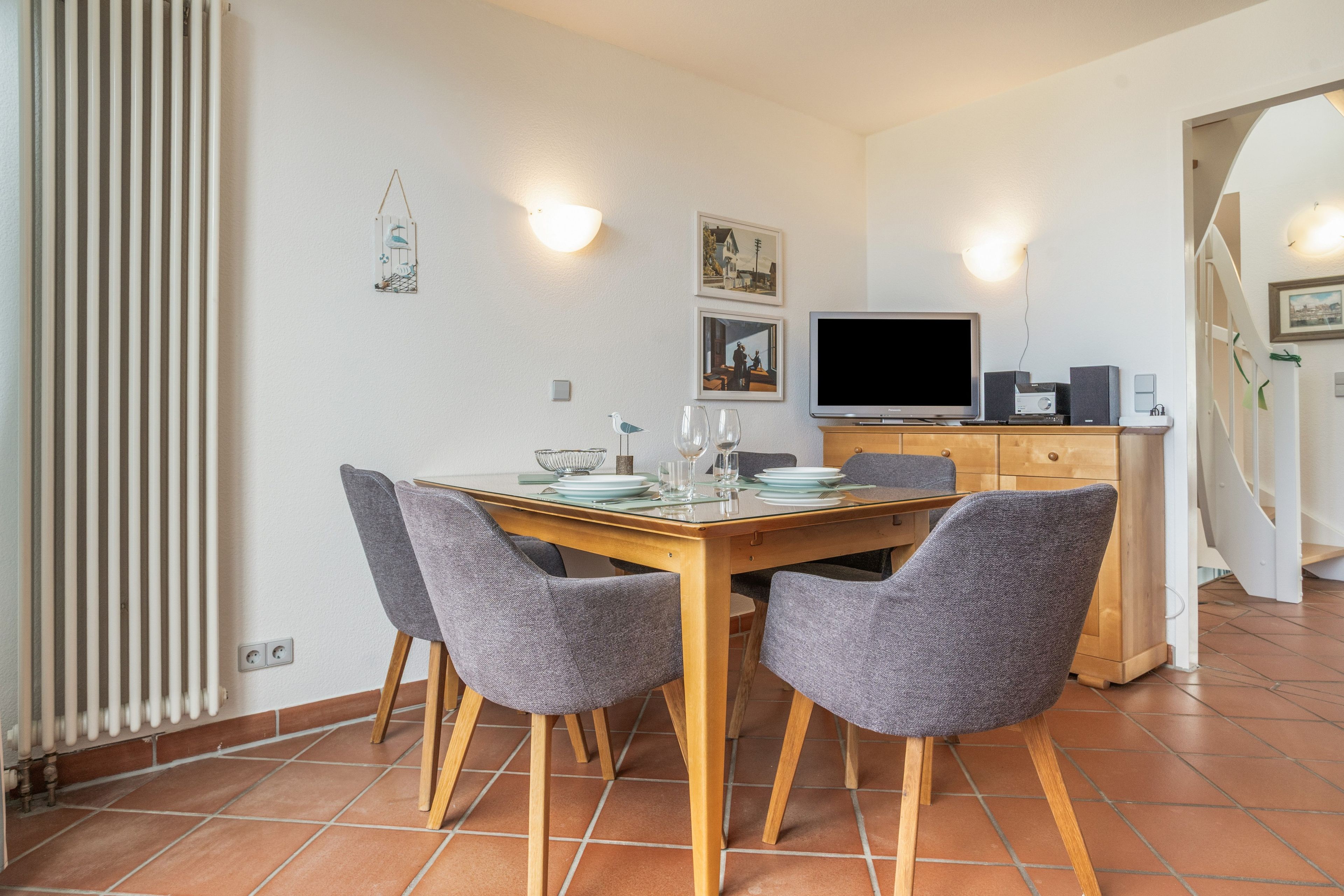 Un coin repas comprenant une table en bois, quatre chaises grises, un téléviseur et un meuble.