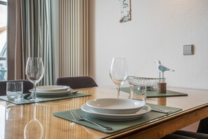 Une table à manger dressée avec des assiettes, des verres et des couverts, et une sculpture d’oiseau accrochée au mur.