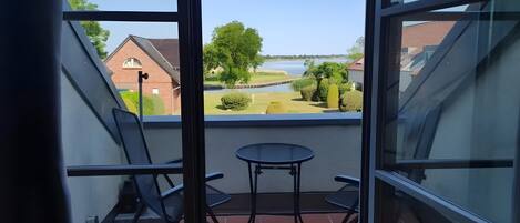 Un balcon avec une table et des chaises, donnant sur une étendue d’eau et sur de la verdure.
