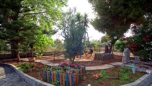 Un jardin avec un chemin de pierres, une clôture en bois et différentes sortes de plantes.