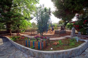 A garden with a stone pathway, a wooden fence, and various plants. - Villa Helios is a country house in a very quiet area, 200 meters from the sea. (Kantia)