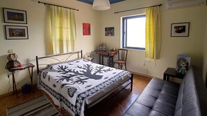 Une chambre à coucher comprenant un lit, un bureau, une chaise, un canapé, une fenêtre avec des rideaux et un climatiseur fixé au mur.