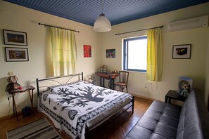 A bedroom with a bed, a desk, a chair, a sofa, a window with curtains, and wall-mounted air conditioning. - Villa Helios is a country house in a very quiet area, 200 meters from the sea. (Kantia)