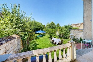 A balcony with a view of a well-maintained garden, a table with chairs, and a blue umbrella. - Villa Sénone – Group Getaway in the Heart of Sens (Sens)