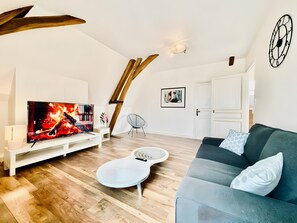 A modern living room with a flat-screen TV, wooden flooring, a white sofa, and a unique ceiling design. - Villa Sénone – Group Getaway in the Heart of Sens (Sens)