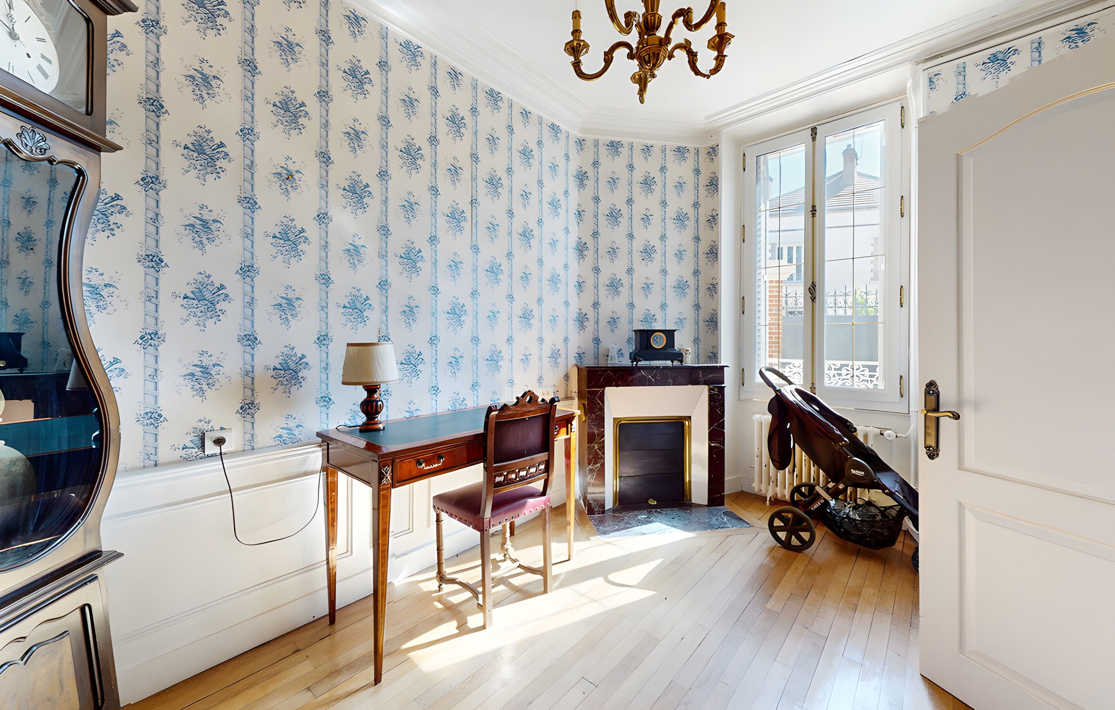 Ein Zimmer mit Holzboden, Kamin, Schreibtisch mit Stuhl, einer Uhr und einem Kinderwagen.
