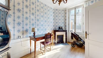 Ein Zimmer mit Holzboden, Kamin, Schreibtisch mit Stuhl, einer Uhr und einem Kinderwagen.