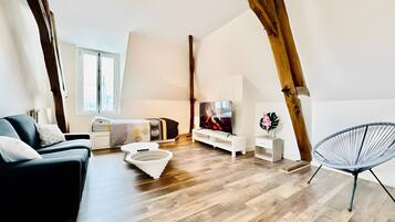 A modern loft-style room with exposed wooden beams, a black sofa, a white bench, a TV, and a hanging chair.