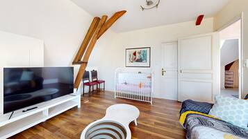 Un salon avec une télévision, un berceau blanc, un canapé et un escalier en bois.