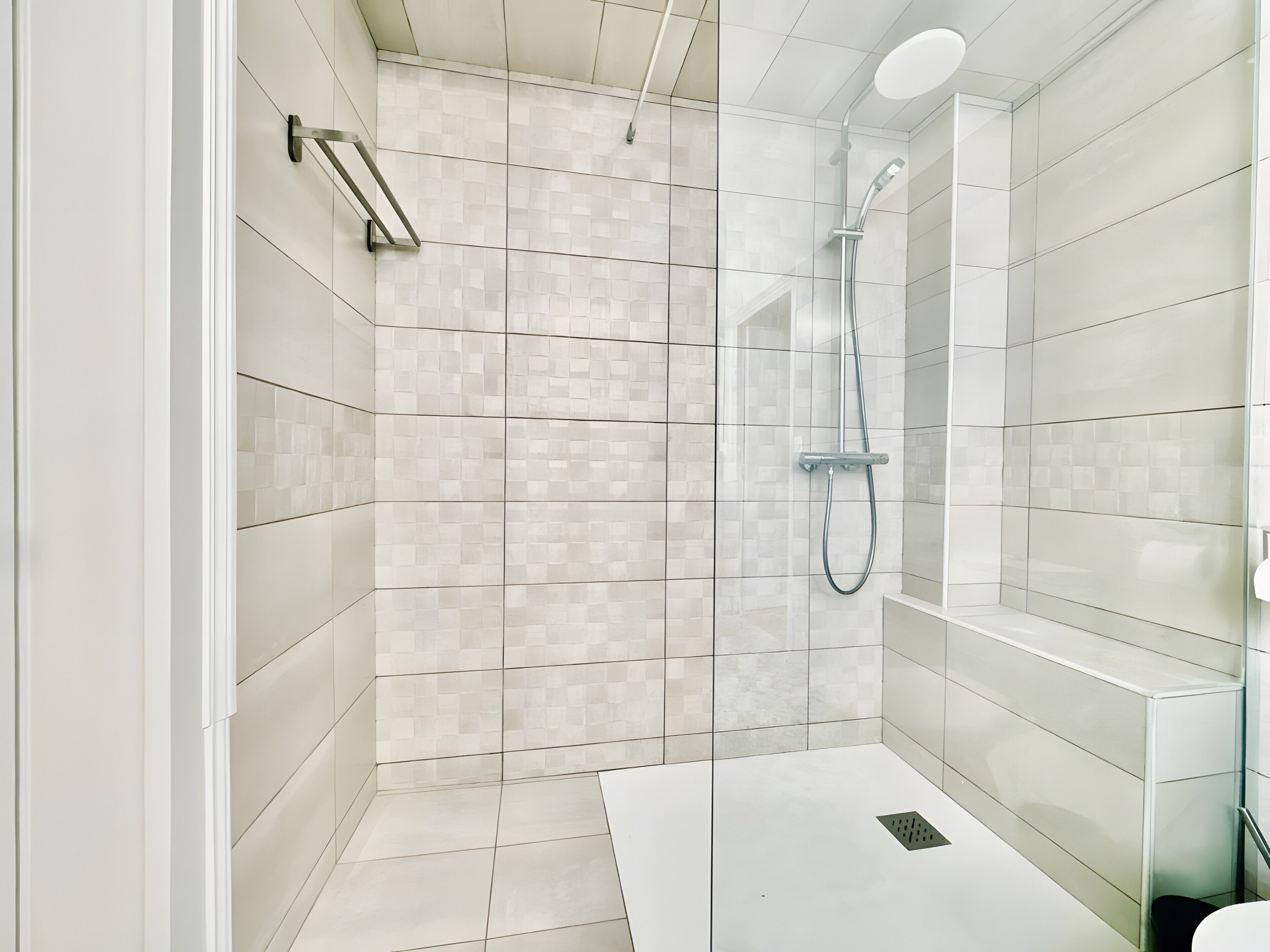 Una ducha moderna con puerta de vidrio, paredes con azulejos y piso blanco.