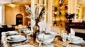 A dining table set with white plates, glasses, and cutlery, a vase with dried pampas grass, and a chandelier.