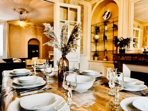 A dining table set with white plates, glasses, and cutlery, a vase with dried pampas grass, and a chandelier. - Villa Sénone – Group Getaway in the Heart of Sens (Sens)