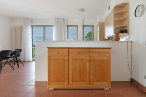 Une cuisine avec des meubles en bois, un plan de travail blanc et une vue sur l’extérieur grâce à de grandes fenêtres.