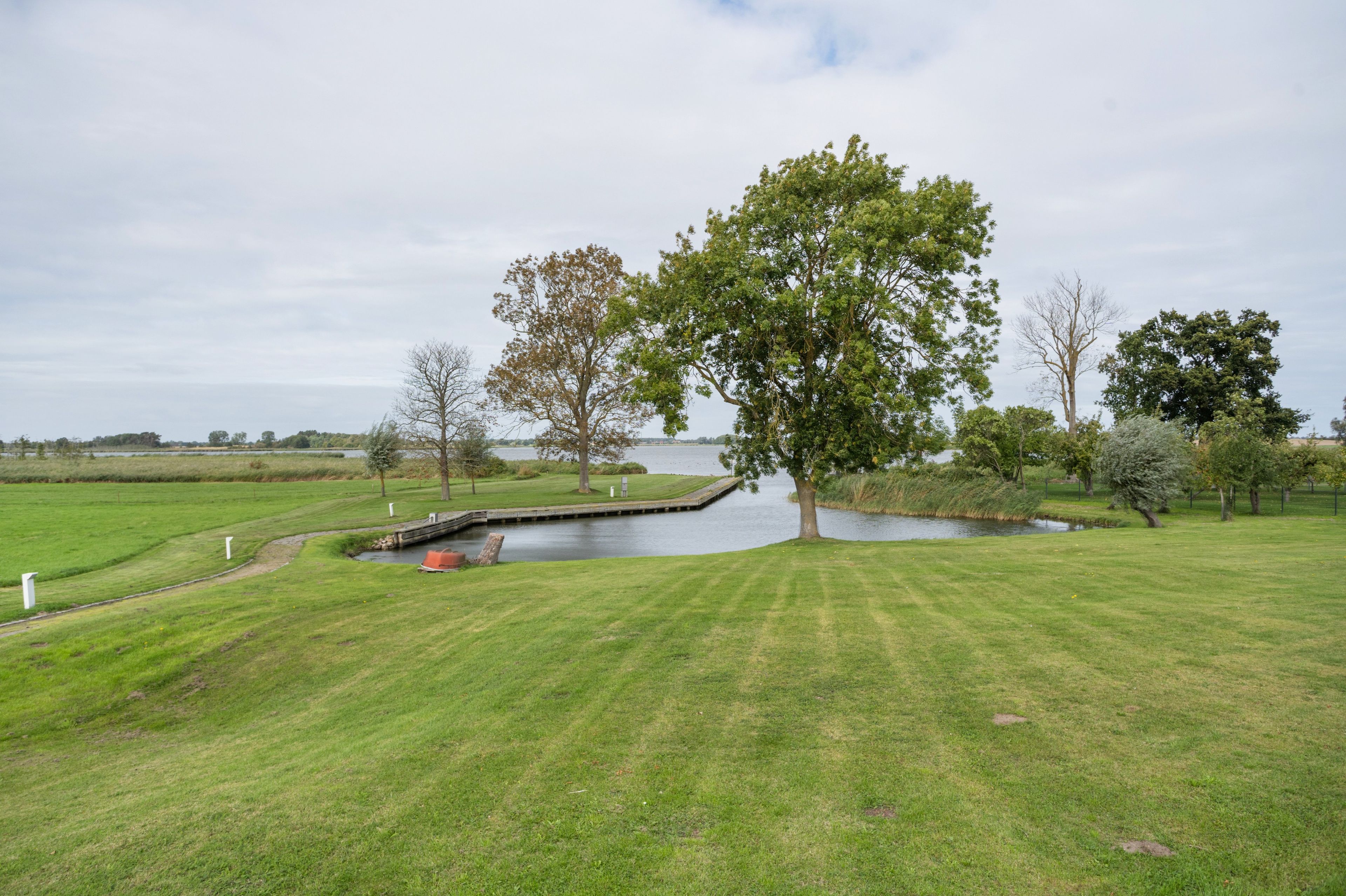 Eine grüne Landschaft mit Teich, Bäumen und einer Holzbrücke.