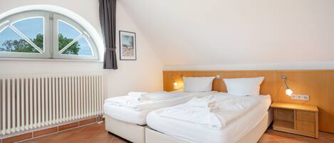 A bedroom with a double bed, a bedside table, a nightstand, a window with a view, and a radiator.