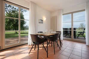 A dining area with a table set for four, large windows, and a view of the outdoors. - Holiday Home 'Waterkant' – Family-Friendly House with Large Terrace (Mellenthin)