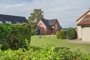 A residential property with a well-maintained lawn, a blue door, and a brick house with a sloped roof. - Holiday Home 'Waterkant' – Family-Friendly House with Large Terrace (Mellenthin)