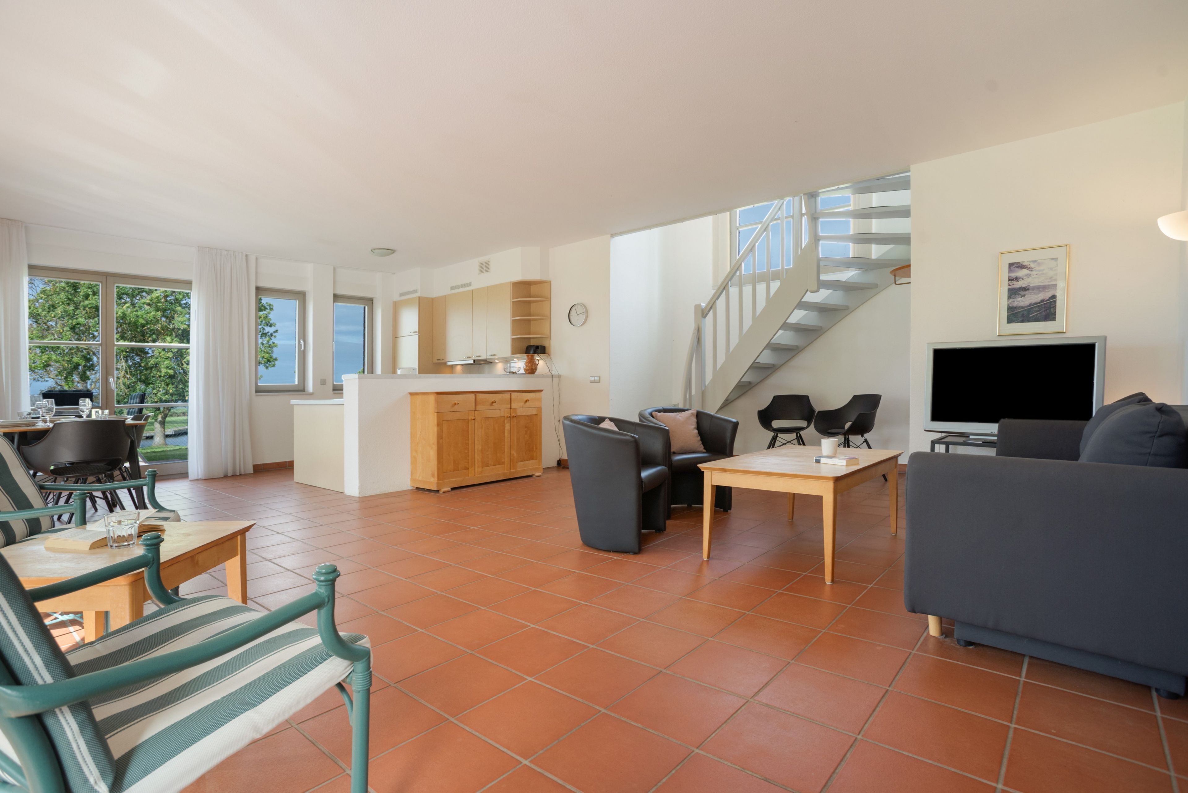 A spacious living area with a dining table, sofa, and a staircase leading to an upper level.