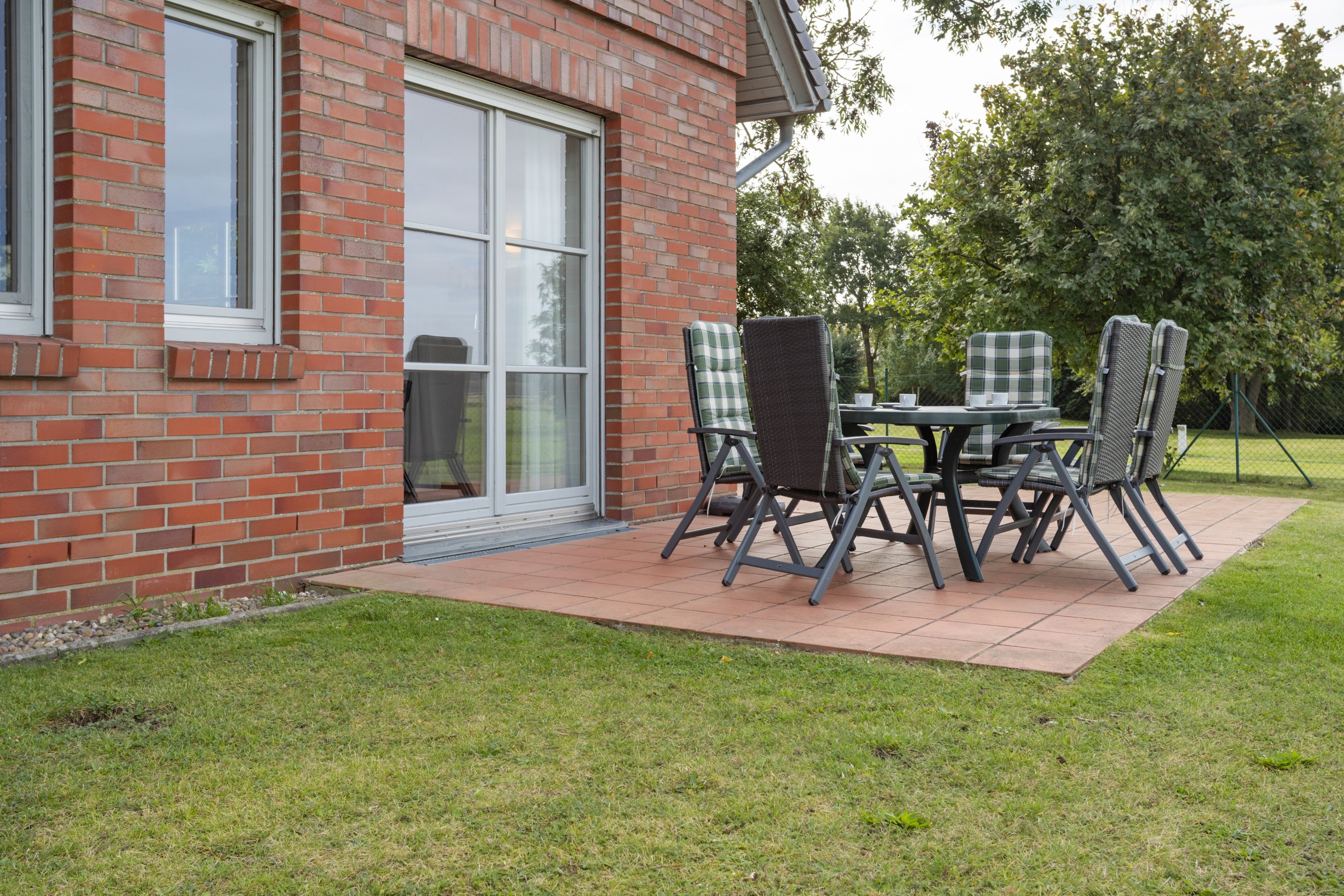 A patio with a table and chairs, a brick building, and a grassy area.