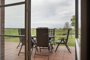 A patio with wicker furniture and a view of a grassy field. - Holiday Home 'Waterkant' – Family-Friendly House with Large Terrace (Mellenthin)