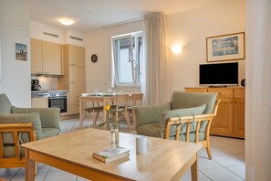 Ein modernes Wohnzimmer mit Esstisch, Stühlen, einem Fernseher und einer Küche im Hintergrund.