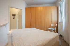 Une chambre à coucher avec un lit, une armoire en bois, une chaise et une fenêtre.